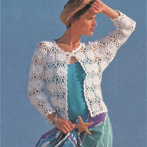 May include: White crochet cardigan with a delicate openwork pattern. The cardigan has a V-neck and long sleeves. The model is wearing the cardigan over a turquoise tank top and a colorful scarf.