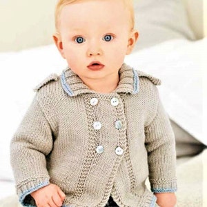 Op de afbeelding: Een baby draagt een beige gebreide cardigan met blauwe bies en knopen. De cardigan heeft een matrozenkraag en is aan de voorkant dichtgeknoopt.