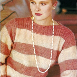 Può includere: Una donna indossa un maglione a righe rosa e bianche con una collana di perle.