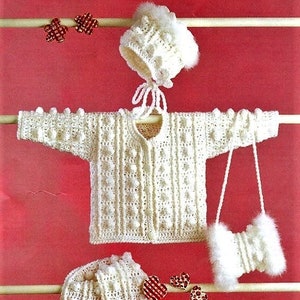 May include: A white crocheted baby outfit set including a cardigan, hat, and a small purse. The set is decorated with white bobbles.