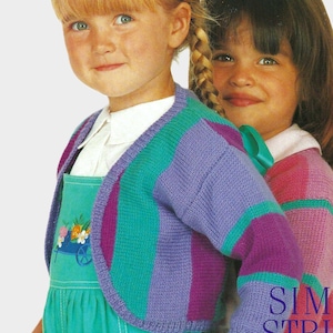 May include: A knitted cardigan featuring vertical stripes in shades of purple, teal, and magenta. The garment has long sleeves and a rounded neckline. It is worn over a white collared shirt and a teal overall dress with a floral wheelbarrow graphic.