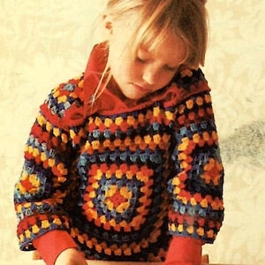 Puede incluir: Una persona joven lleva un suéter de ganchillo colorido con un patrón geométrico. El suéter está hecho con hilo rojo, amarillo, azul y naranja. La persona está jugando con bloques de madera.