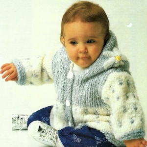 May include: A baby wearing a blue and white knitted cardigan with a flower on the hood. The cardigan has a button closure and is made with a soft, fluffy yarn.