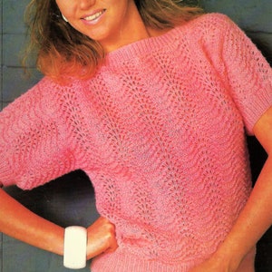 May include: A pink knitted sweater with a lacy pattern. The sweater has short sleeves and a round neckline. The sweater is sized 81-107 cm.