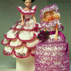 Puede incluir: Dos muñecas con vestidos blancos y rosas hechos a mano. Los vestidos tienen bordes festoneados y están adornados con cintas y flores. Una muñeca lleva un sombrero a juego. Las muñecas están sobre una superficie blanca.