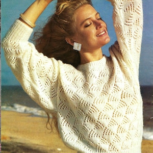 May include: A white crocheted sweater with a delicate openwork pattern. The sweater has a round neckline and long sleeves. The model is wearing the sweater with her arms raised above her head, showing off the intricate design.