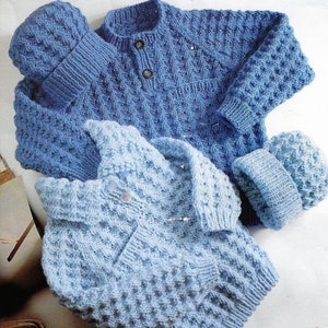 May include: Two blue knitted baby cardigans with matching hats. The cardigans have a textured stitch pattern and button fastenings.