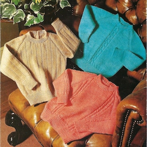 May include: Three knitted sweaters in beige, teal, and coral sit on a leather chair. The beige sweater has vertical ribbing, the teal has a cable knit design, and the coral has diagonal ribbing. The sweaters are examples of handmade knitwear.