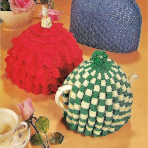 Puede incluir: Tres cubre-teteras de ganchillo. Uno es rojo con un diseño de volantes, otro es de rayas verdes y blancas, y el último es azul con un patrón de rombos.