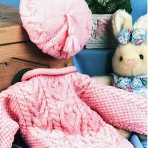 May include: A pink knitted baby sweater and matching beret with a cable knit pattern. The sweater has a high collar and long sleeves. The beret has a tassel.