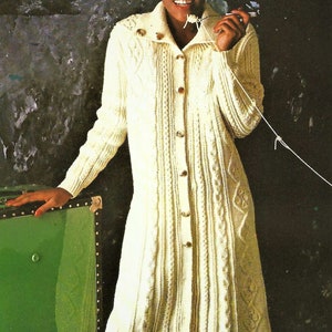 May include: A white knitted cardigan with a cable knit pattern and button closure. The cardigan is long and has a collar.