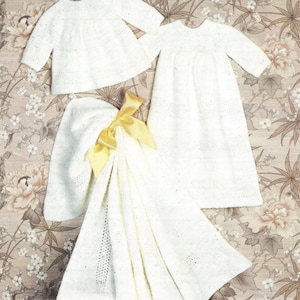 Peut inclure: Ensemble de vêtements de bébé en tricot blanc, comprenant un haut à manches longues, une robe, un bonnet et une couverture. La couverture est ornée d'un ruban jaune. Les articles sont présentés sur un fond à motifs floraux.
