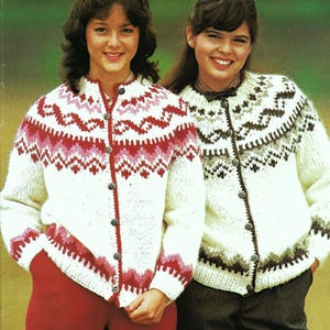 May include: Two people wearing white knit cardigans with patterned designs. One cardigan features red and pink patterns, while the other has brown and gray patterns. Both cardigans have button closures and are worn with pants.
