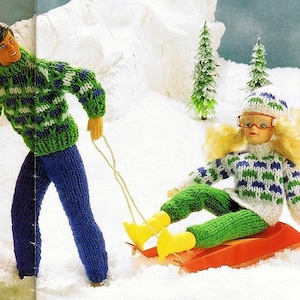 Puede incluir: Un suéter de color verde y blanco con un patrón y pantalones azules para una muñeca. Un suéter de color verde y blanco con un patrón y pantalones azules para una muñeca. La muñeca lleva un sombrero blanco con un patrón verde y blanco y gafas rojas. La muñeca está sentada en un trineo rojo.