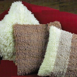May include: Three decorative throw pillows with a fluffy, textured fabric. The pillows are in shades of white, brown, and beige.