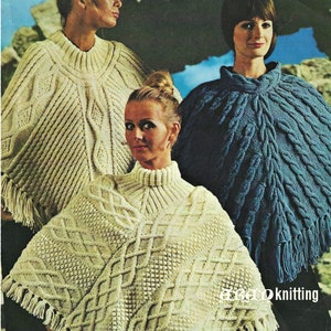 Peut inclure: Trois femmes portant des ponchos tricotés différents. Les ponchos sont tous blancs, bleus et ont un motif en tricot torsadé. Les femmes sont debout devant un fond rocheux.