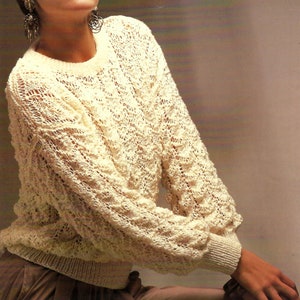 May include: A white crocheted sweater with a delicate openwork pattern. The sweater has long sleeves and a round neckline.