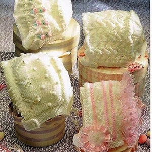 Könnte beinhalten: Vier weiße gehäkelte Babyhauben mit verschiedenen Mustern und Verzierungen, präsentiert auf Holzkisten mit rosa und weißen Akzenten. Die Häubchen sind mit rosa und weißen Blumen und Spitze verziert.