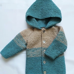 May include: A teal and beige knitted baby cardigan with a hood and button fastening.