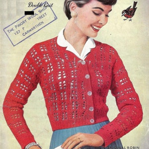 Peut inclure: Un cardigan rouge en tricot avec un motif ajouré. Le cardigan a une fermeture boutonnée à l'avant et des manches longues. Le mannequin porte une blouse blanche sous le cardigan.