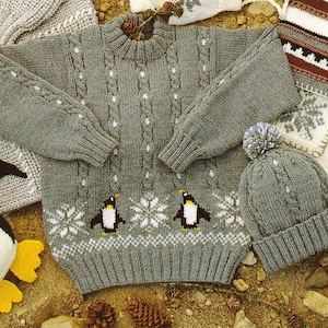 May include: A grey knitted jumper with a snowflake and penguin design. The jumper has a cable knit pattern and a ribbed collar. A matching grey knitted hat with a pom-pom is also pictured.