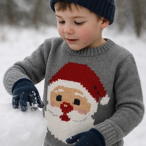 May include: A child in a grey Santa Claus sweater, navy blue hat and gloves, building a snowman. The sweater has a red hat and white beard design. The scene is set outdoors in the snow. The child is wearing a knitted hat.