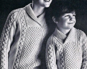 May include: Two children wearing white knitted sweaters with a cable knit pattern. The sweaters have a v-neck collar. The boy on the left is wearing a white knit hat. The image includes the text "9d 1096" and "Sizes 22 to 32".