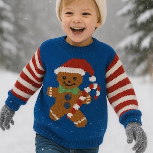 Puede incluir: Un niño con un jersey navideño azul con un diseño de hombre de jengibre, mangas a rayas rojas y blancas y un gorro crema. El niño sonríe, con guantes grises, con nieve cayendo al fondo.