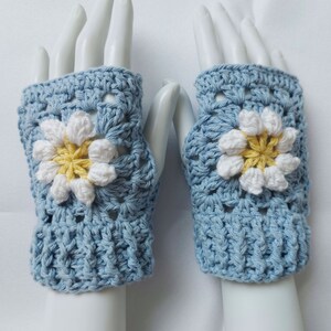May include: A pair of light blue crocheted fingerless gloves with a white daisy flower design. The flowers have yellow centers.