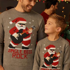 May include: Two gray sweaters with a Santa Claus design playing a guitar. The Santa is wearing a red hat and suit. The text "JINGLE BELL ROCK" is below the Santa graphic. The sweaters are worn by a man and a boy.