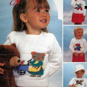 Peut inclure: Un pull en tricot blanc avec un motif brodé coloré représentant une fille poussant un chariot à jouets avec un ours en peluche. Le pull est porté par une jeune fille aux cheveux roux et un nœud rouge. Elle tient un ours en peluche brun.