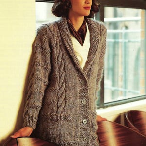 May include: A long-sleeved, knitted cardigan with a cable knit pattern and a large collar. The cardigan is a light brown color and has a button closure.