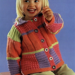 May include: A young child wearing a colorful knitted cardigan with a button closure. The cardigan has a patchwork design with squares of pink, purple, green, and yellow yarn.