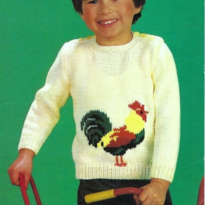 May include: A white knitted sweater with a colorful rooster design on the front. The rooster is red, yellow, green, and black.