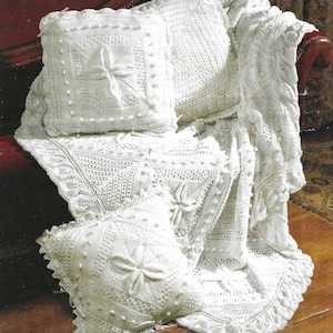 May include: Three white crocheted cushions with a floral design, one is a throw cushion and the other two are square cushions. The cushions are on a white crocheted throw blanket.