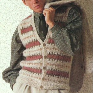 May include: A man is wearing a cream, pink and brown patterned knitted waistcoat with a button-up closure. He is also wearing a green plaid shirt and beige trousers.