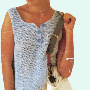 May include: A light blue sleeveless knitted top with a button closure and a white strap. The top is worn with white pants.