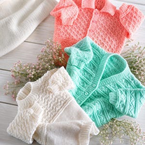 Puede incluir: Tres jerséis de punto en color coral, verde menta y crema. Los jerséis coral y verde menta cuentan con una parte delantera abotonada con cuello y un patrón de rombos texturizado. El jersey crema tiene un cuello redondo y diseño de punto.