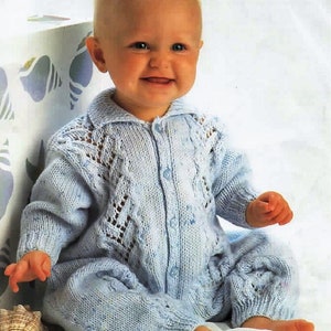 May include: A light blue knitted baby romper with a collared neckline and button-up front. The romper features intricate openwork detailing on the chest and sleeves. The baby is smiling and sitting on a white surface.