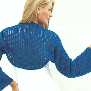 May include: A blue crochet shrug with long, flared sleeves. The open-weave design of the bolero-style top is visible. The garment is worn over a white top, creating a contrast. The sleeves are approximately 24 inches long.