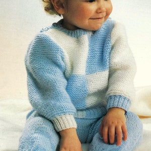 May include: A baby wearing a blue and white knitted sweater and matching pants. The sweater has a checkered pattern.