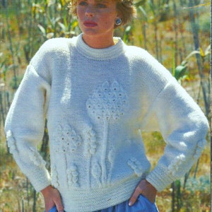 Könnte beinhalten: Ein weißer Strickpullover mit Blumenmuster. Der Pullover hat einen Rundhalsausschnitt und lange Ärmel. Das Blumenmuster besteht aus weißem Garn und hat die Form von Blumen und Blättern.