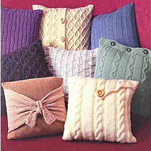 May include: A collection of knitted throw pillows in various colors and patterns, including a brown pillow with a bow, a white pillow with a button, and a green pillow with a cable knit design.
