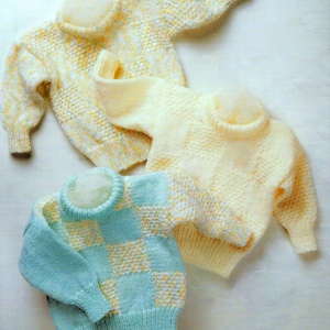 May include: Three knitted baby sweaters in different colors and patterns. One is yellow with white flecks, one is cream with white flecks, and one is blue and white checkered.