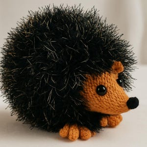 May include: A knitted hedgehog toy with a black and gold spiky back, a tan face, and small black eyes. The hedgehog has small tan feet and a black nose. This soft toy is suitable for children.