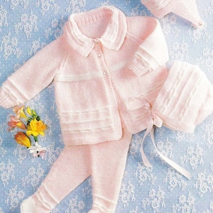May include: A pink knitted baby outfit with a cardigan, pants, and a bonnet. The outfit has white trim and buttons.