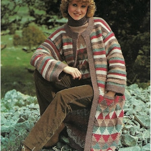May include: A long, striped cardigan with a geometric pattern on the front and a matching hat. The cardigan is brown, pink, green, and white. The model is wearing brown pants.