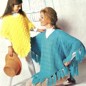 May include: A woman and a girl wearing matching knitted ponchos. The woman's poncho is turquoise blue with fringe and the girl's poncho is yellow with fringe.