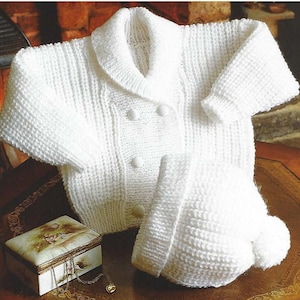 May include: A white knitted baby cardigan with a collar and button closure, paired with a matching white knitted hat with a pom-pom.