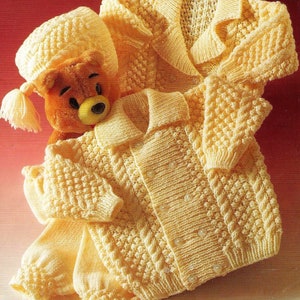May include: A yellow knitted baby cardigan, hat, and pants set. The cardigan has a button closure and a cable knit pattern. The hat has a tassel.